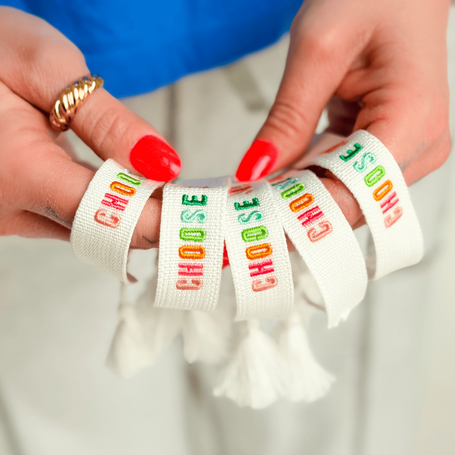 Choose Joy embroidered bracelet with colorful text on a cream fabric, held in a hand with red nails.