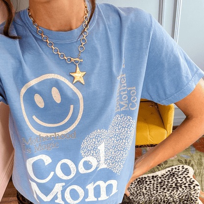 Gold star charm necklace worn over a blue graphic t-shirt with a smiley face and text.