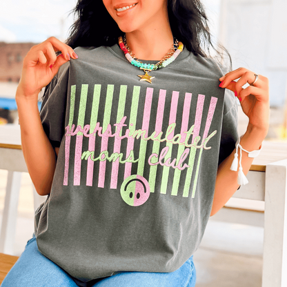 Overstimulated Moms Club tee in gray with colorful striped design and smiley face graphic, worn by a woman.