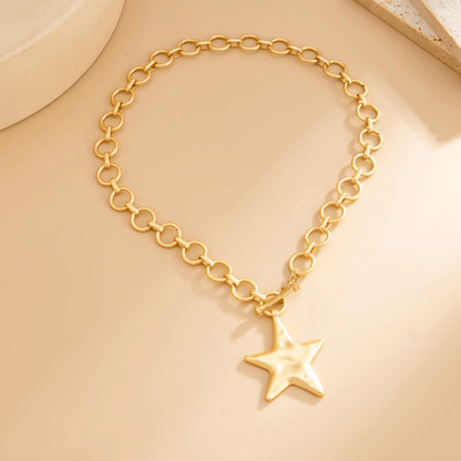 Gold star charm necklace with a chunky gold chain and a polished star pendant on a beige background.