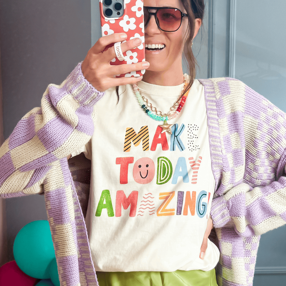 Person wearing a colorful 'Make Today Amazing' shirt in a room with balloons and a mirror.